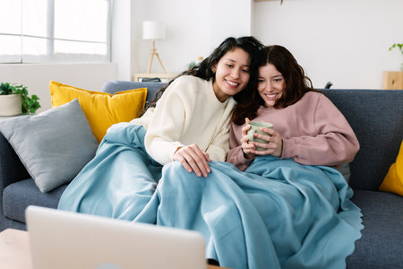 Happy multiracial young female friends watching movie on laptop