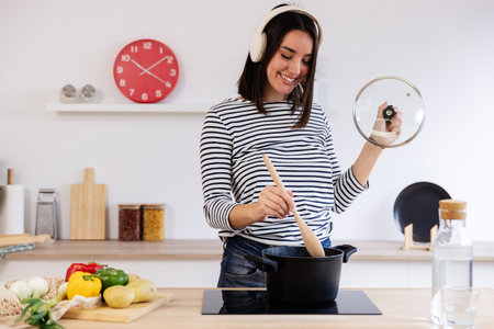 Young happy woman enjoying music while cooking in the kitchen at homeの写真素材