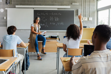 Rear view of young student girl raising her hand to ask a question in class