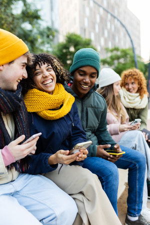 Happy young students using smart phones at city street on winterの写真素材