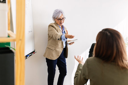 Senior businesswoman leading a presentation in modern office with colleagues interactingの写真素材