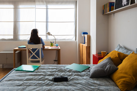 Rear view of young teen student girl working on laptop in her bedroomの写真素材