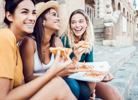 Happy young women tourists eating italian pizza enjoying summer vacationの写真素材