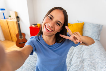 Teenage girl smiling and making peace sign selfie at homeの写真素材