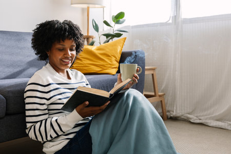 Young African American woman reading a book in winter morning at home