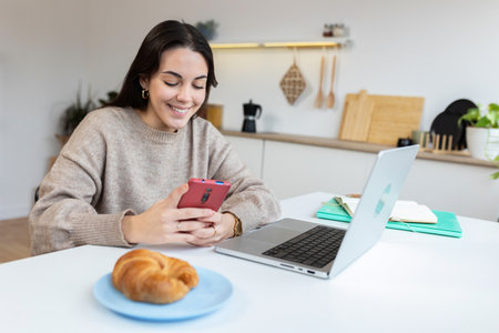 Young happy student woman using mobile phone while studying on laptopの写真素材