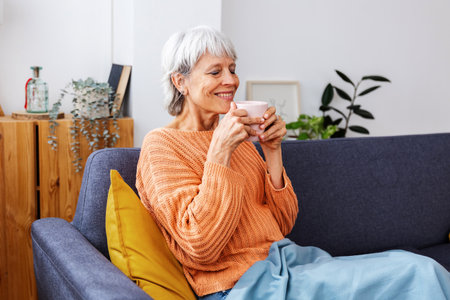 Portrait of middle-aged woman enjoying aroma coffee sitting on sofa in winterの写真素材