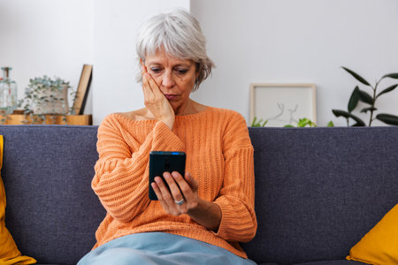 Senior woman feeling concerned reading bad news on smart phone messageの写真素材