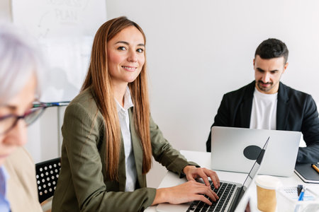 Businesswoman typing on laptop during meeting with colleagues in officeの写真素材