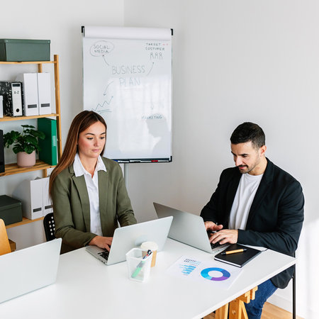 Business people working on laptops in modern office with business plan on whiteboardの写真素材