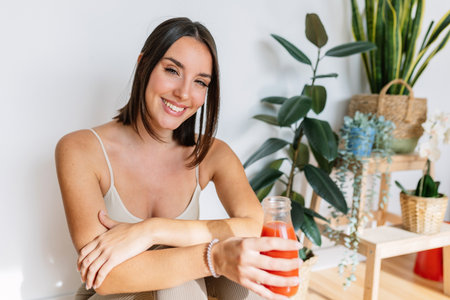 Smiling portrait of young pretty woman enjoying homemade healthy juice at homeの写真素材