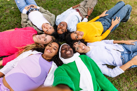Happy group of women lying on circle on grass taking selfie portrait at park.の写真素材