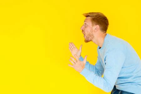 Young man shouting and gesturing on yellow backgroundの写真素材
