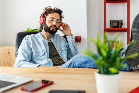 Relaxed man listening to music with headphones while taking a break from work.の写真素材