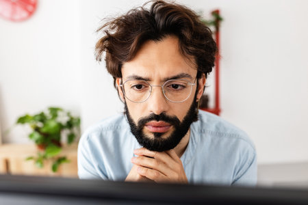 Young bearded man in glasses working concentrated on laptop computer from homeの写真素材