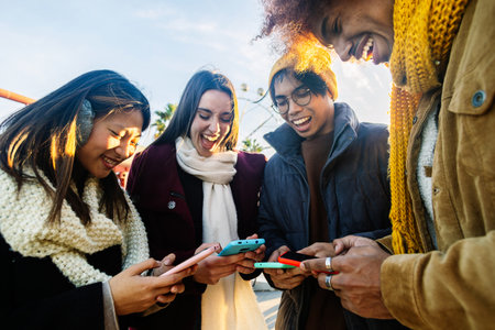 Young group of people in warm clothes using mobile phone device on winterの写真素材