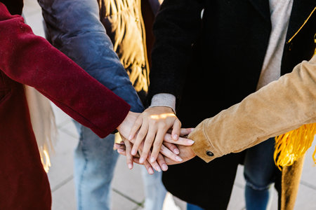 Friends showing teamwork by joining hands together in winterの写真素材