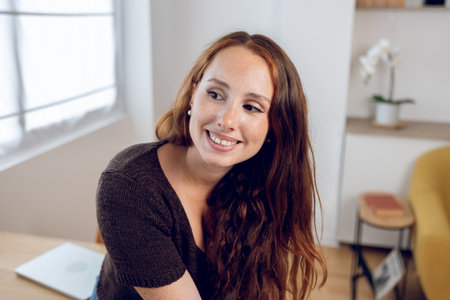 Portrait of young happy woman sitting at home office table in cozy workspaceの写真素材