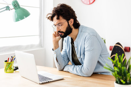 Concentrated young businessman working on laptop computer at home officeの写真素材
