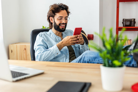 Young adult handsome man using smart phone device sitting at deskの写真素材