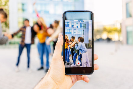 Hand holding smart phone capturing friends having fun together in lively city