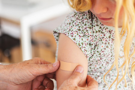 Doctor stick band aid on little girl shoulder after vaccination at hospital