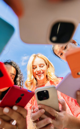 Smiling young women looking at smartphones outdoors