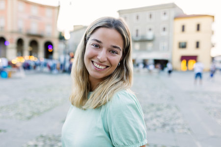 Happy young blonde woman smiling at camera standing at city street.の写真素材