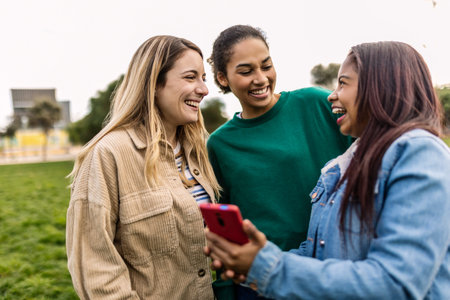 Three young female friends having fun using smart phone outsideの写真素材