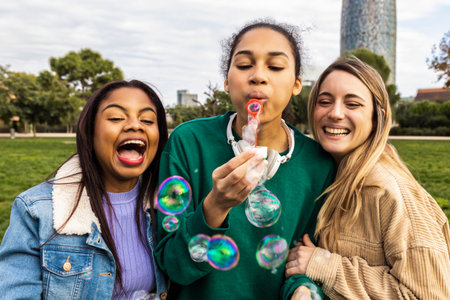 Diverse girls friends having fun blowing bubbles in parkの写真素材