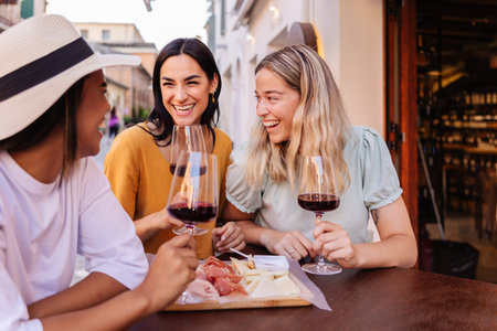 Happy young women sharing red wine at cafe table