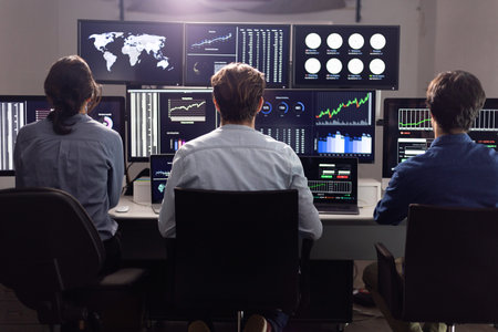 Stock traders working on multiple computer screens showing charts and graphs