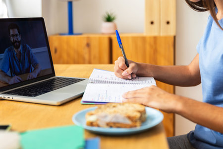 Teenage student girl following online class on laptop and taking notes