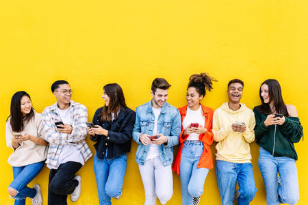 Young group of people having fun using mobile phone over yellow wall
