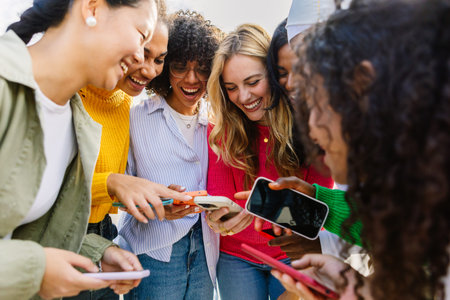 Group of female friends having fun using mobile phones outdoors