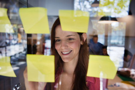 Woman brainstorming creative ideas on a glass wall with sticky notes
