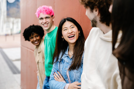 Diverse young friends smiling and chatting near wall outdoors