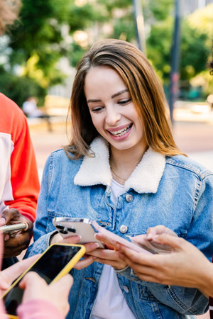 Young happy woman checking smartphone with friends in urban park