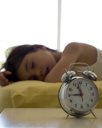 little girl on the bed with an alarm clockの写真素材