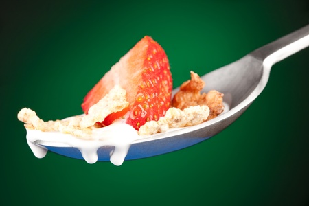 spoon with flakes and strawberry on green background