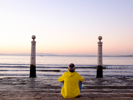 man sitting and watching the ocean at sunrise in Cais das Colunas, Lisbon, Portugalの写真素材