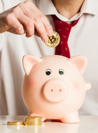 businessman putting bitcoins into a piggy bank isolated on white backgroundの写真素材