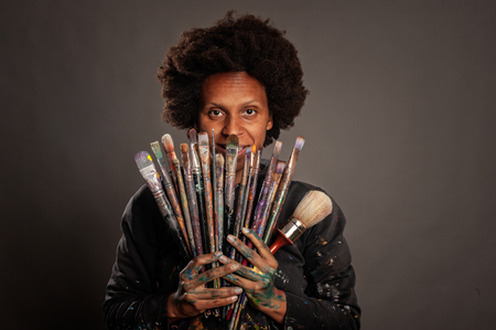 happy black woman holding paintbrushes on a gray backgroundの写真素材