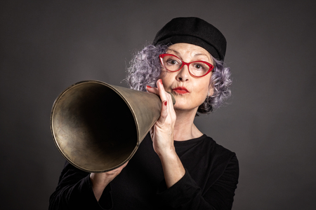 portrait of beautiful older woman shouting with an old megaphone on a gray backgroundの写真素材