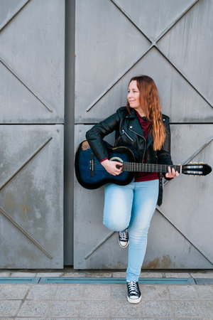 Street musician playing acoustic guitar. Young woman wearing jacket outdoorsの写真素材