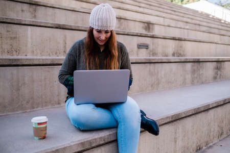 Portrait of freelancer woman using laptop while sitting on stairs in city street. Blogger concept.の写真素材