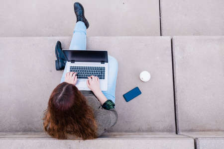 Portrait of freelancer woman using laptop while sitting on stairs in city street. Blogger concept.の写真素材
