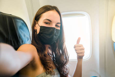 girl wearing face mask taking selfie with smartphone while sitting on airplaneの写真素材