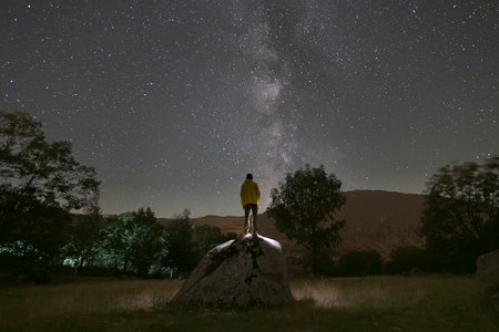 rear view of man climbed on a rock looking at the milky way at nightの写真素材
