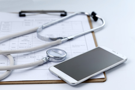 Mobile phone, stethoscope and chart file on the desktop (mobile medical, handheld doctor concepts)の写真素材